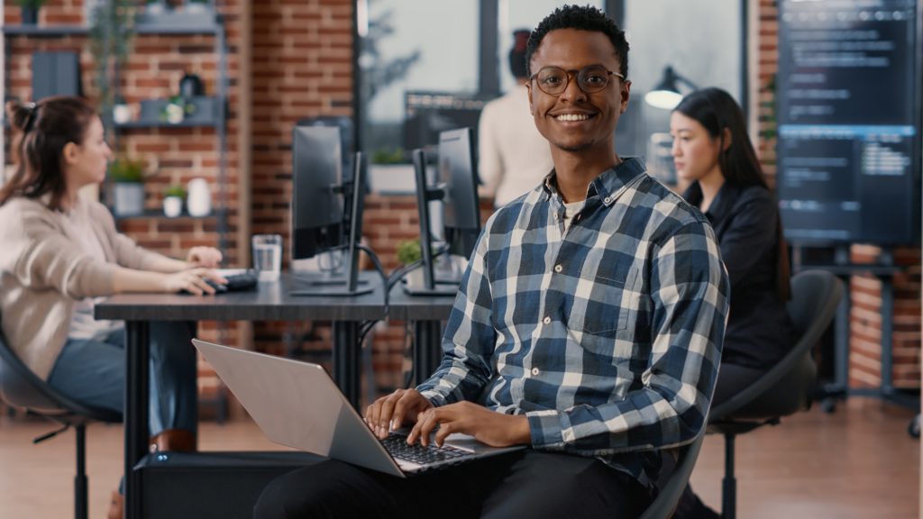 Portrait of artificial intelligence app developer sitting down typing on laptop fixing glasses