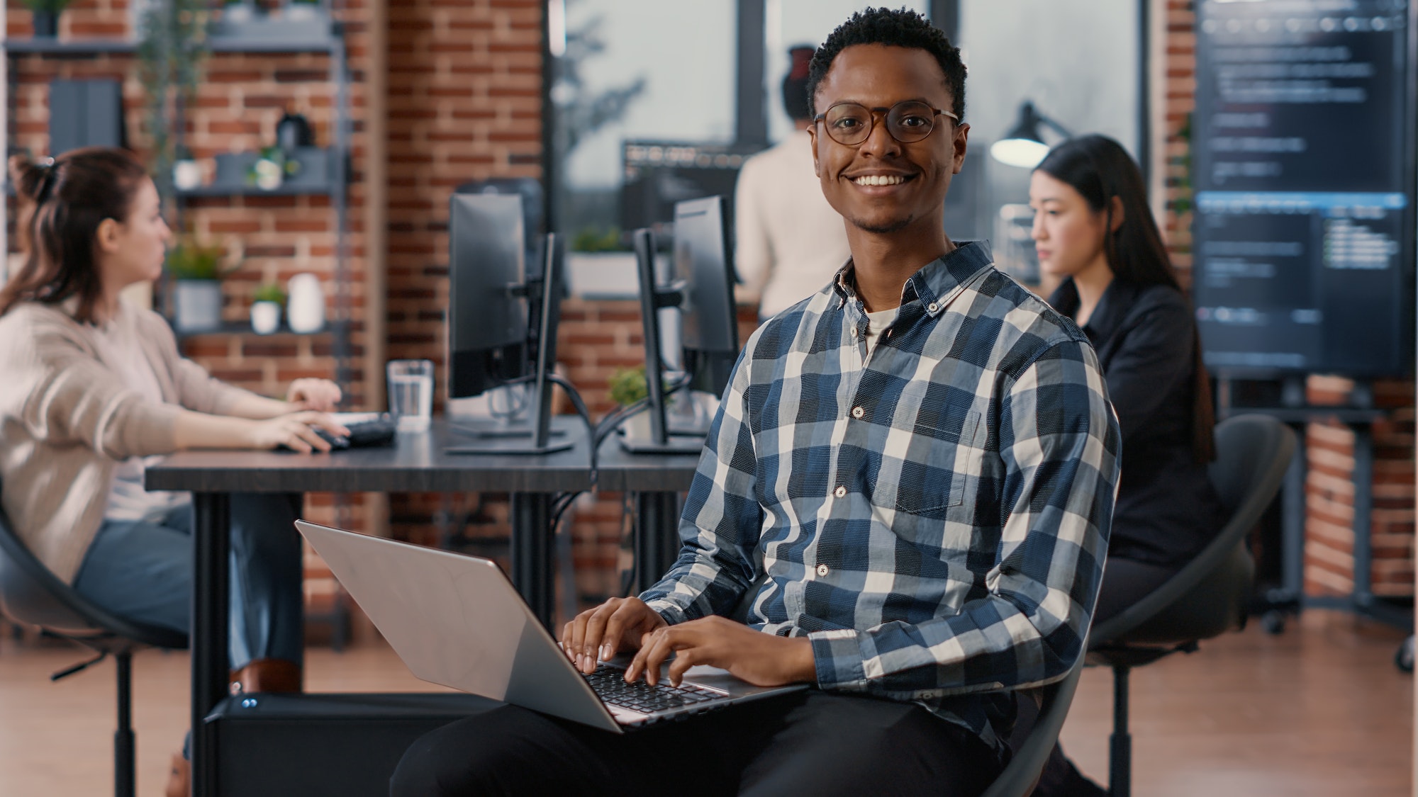 Portrait of artificial intelligence app developer sitting down typing on laptop fixing glasses